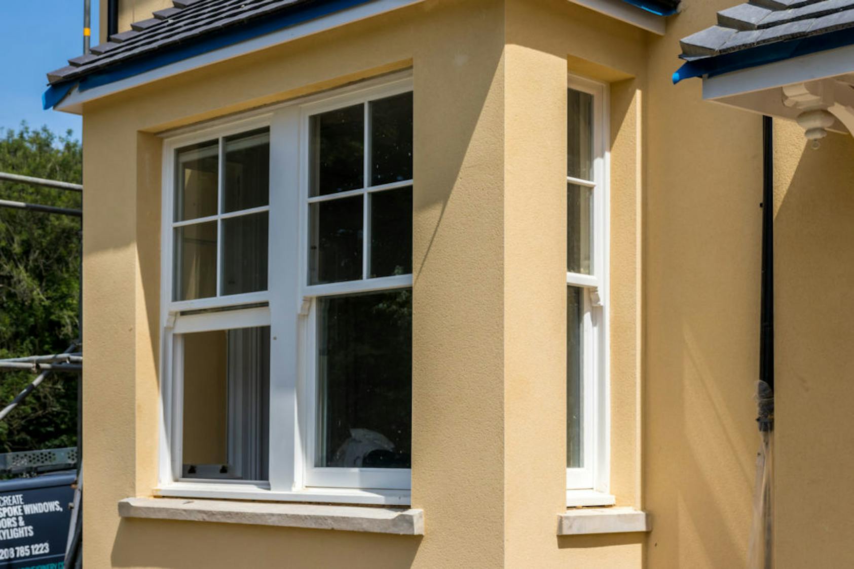 White wooden sash windows on a yellow-painted house exterior with classic bay window design.
