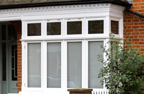 Traditional bay window with white wooden frame and decorative top panels on brick exterior.