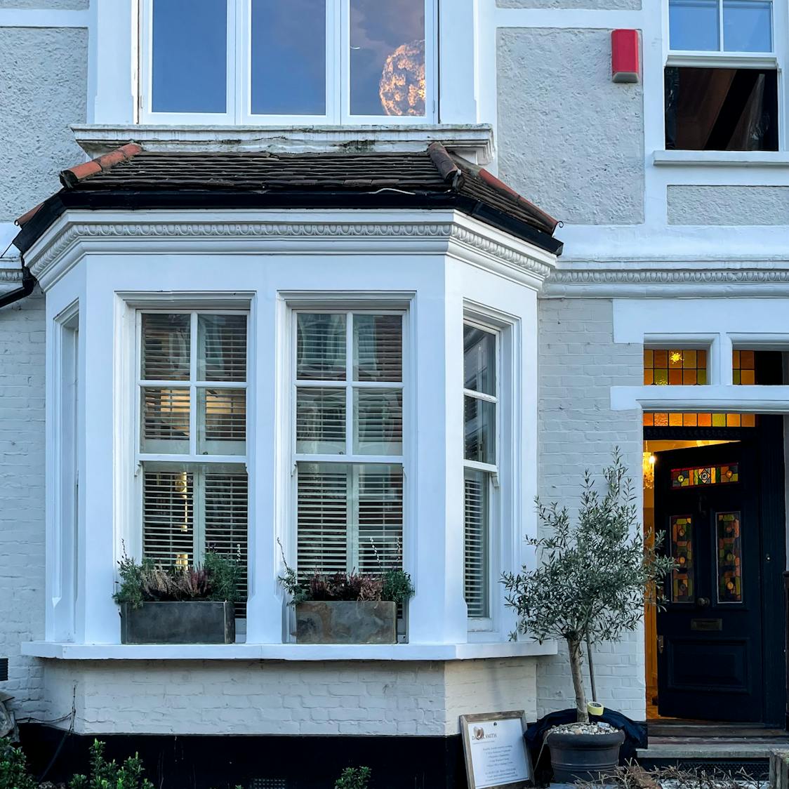 Traditional bay window with white wooden frames and decorative grid design on the exterior of a period house.