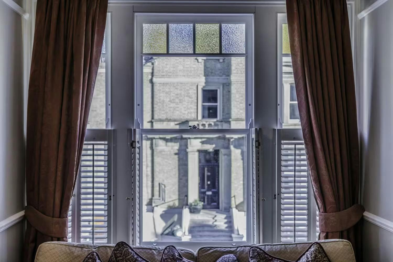 shuttters and floor to ceiling curtains on an edwardian sash window with stained glass